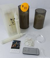 Photo of flameless LED candles, smoky cylindrical holders, remote, packaging box, adhesive pads, instruction sheet, and plastic ring.