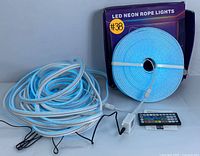 Photo of coiled LED neon rope light emitting a blue glow, showing the remote control and power adapters included.