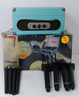 Turntable unit in turquoise case on top of original box with black detachable legs arranged in front.