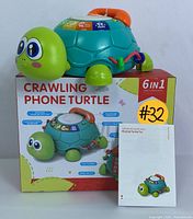 Front view of the 6-in-1 Crawling Phone Turtle toy on top of the original packaging box with instruction manual propped beside it.