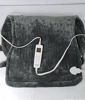 Gray plush electric heated shoulder wrap laid flat showing shape and attached white digital control and power cord.