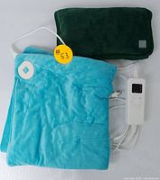 Two electric heating pads with plush covers; turquoise and dark green colors, controllers attached.