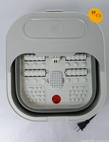 Top-down photo of the light gray electric foot spa showing massage rollers, textured footbed, red heating indicator light, and power cord.
