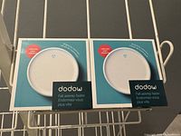Two boxed white circular Dowdow sleep aid devices side-by-side on a wire shelf, packaging showing front design and branding.