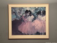 Framed print artwork showing ballerinas mostly on the right side wearing pink tutus, with a dark and textured background, framed in a light-colored mat and wooden frame.