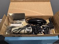 Box containing hair clippers, attachments, scissors, and combs, all organized inside a cardboard box.
