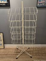 Full view of the white metal magazine display rack showing its overall structure, wire compartments on both sides, and wheeled base.