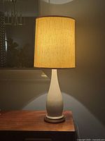 Full view of the lamp illuminated, showing ceramic base with walnut platform and fabric shade