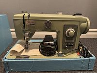 Side view of the beige Brother Pacesetter heavy-duty vintage sewing machine on a blue box, showing the front dials and foot pedal.
