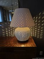 Lit view of the white perforated ceramic table lamp casting patterned light on surrounding surfaces.