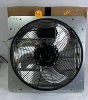 Front view showing square mounting frame, metal fan blades covered by black wire guard, and wiring.
