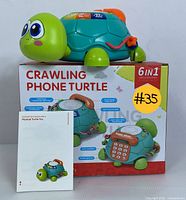 Front view of the turtle toy on top of its original packaging. The box reads 'Crawling Phone Turtle' and '6 in 1'. Instruction booklet is present in front.