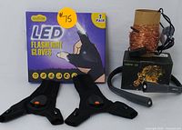 Pair of black Outlite LED flashlight gloves with packaging and lit LED lights on thumbs and index fingers, plus a spool of Lepro LED string lights with black wire and remote control.