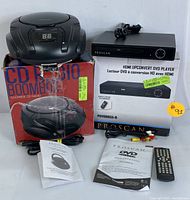 Full view of Proscan CD radio boombox atop its original box alongside Proscan HDMI upconvert DVD player with remote, cables, manuals, and boxes visible.