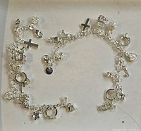 Two charm bracelets laid out in a circular fashion showing various dangling charms like crosses, hearts, stars, rings, and textured shapes on a silver tone chain.