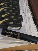 Six black boxes labeled Statement Brow Brow Gel from Elizabeth Arden alongside one brow gel stick tube shown with brand text Elizabeth Arden New York.