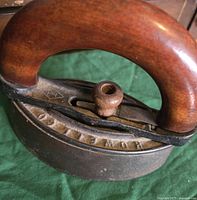 Close-up side angle of antique sad iron showing wooden handle and PATENT embossed on iron base.