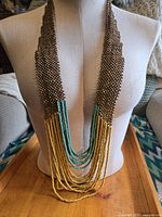 Front view of a long multi strand bohemian style necklace on a dress form, showing the bead colors and woven section clearly.