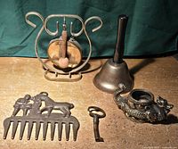Full view of all brass items together on wooden surface: horse comb, gong, bell, key, dragon figurine.