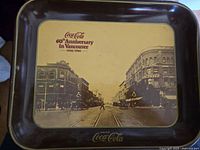 Front of commemorative Coca-Cola tray showing Vancouver street scene and anniversary text, with some wear visible.