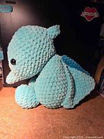 Side angle view showing the crochet texture, small wings, snout, and black eyes of the turquoise pterodactyl plush.