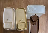 Top view showing the four Tupperware container lids with small measuring cups attached, two beige and two brown.