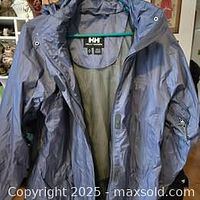 Front view of the Helly Hansen shell jacket with the hood partially visible, showing mesh lining inside and zipper details.