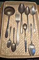 Nine silver utensils arranged on woven tray showing all items clearly.
