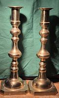 Front view of two tall brass candlesticks with octagonal bases and rounded ornamental shafts.