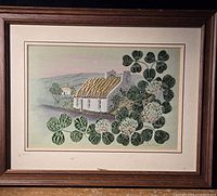 Framed woven textile art showing Irish cottage and large clover leaves with flowers.