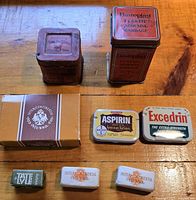 Vintage packaging containers including bandage tins, aspirin and pain reliever tins, soap box and sugar cubes with brand labels as listed.