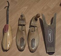 Three wooden shoe stretchers and one wooden shoe horn laid out on a wooden floor, showing a dog-shaped shoe stretcher, two traditional Windsor shoe stretchers, and a Y-shaped Boulet shoe horn.