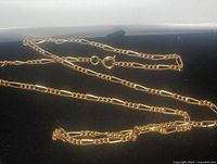 Gold tone Figaro chain necklace laid flat showing chain details and clasp on black background.