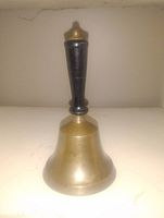 Front view of antique brass school bell with black wooden handle, showing overall shape and surface.