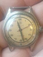 Front view of the antique wristwatch showing cream dial with Arabic numerals and watch hands.