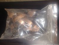 Photo of a sealed plastic bag containing multiple hammered copper cupboard pull handles with a hammered texture.