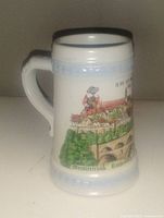 Front view of beer stein showing painted scene of Rothenburg ob der Tauber with buildings, greenery, and a bridge.
