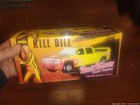 Photo of the front and top side of yellow Kill Bill Pussy Wagon die cast truck box showing branding and image of truck and character.