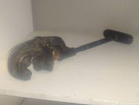 Front angled view of a large antique pipe cutter tool showing the handle, adjustable arm, and cutting wheel mechanism.