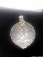 Front side of silver tone pendant showing Buddha figure relief within arch-shaped frame.
