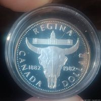 Obverse side of the coin showing bull skull with 'REGINA', 'CANADA', 'DOLLAR', and date range 1882-1982 under Canadian Parliament building graphic.