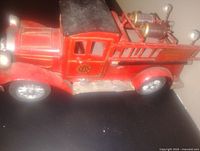 Side view of red metal tin toy fire truck showing details including door emblem, windows, and decorative ladders on side.