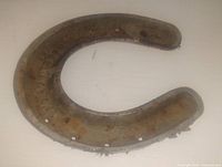 Close-up of the iron horseshoe mold showing rust, holes, and embossed markings on the surface.