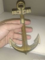 Photo showing the front view of the solid brass anchor wall hanging held in hand to demonstrate size and detail.