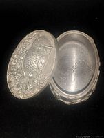 Open oval pewter box showing detailed owl design on lid and smooth interior.
