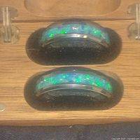 Close-up of the two tungsten rings with blue-green opal inlays inside the wooden box.