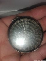 Top side view of the round silver tone makeup compact showing wavy concentric design pattern