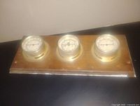 Top view of the wooden plaque showing three round temperature gauges with brass rims and plastic covers.