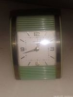 Front view of the clock showing seafoam green ribbed accents and square clock face with black and gold markers.