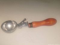 Photo showing the wooden handle, metal scoop, and mechanical lever of the vintage ice cream scoop.